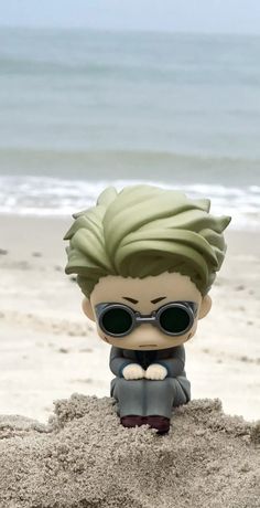 a toy is sitting in the sand at the beach with sunglasses on it's head