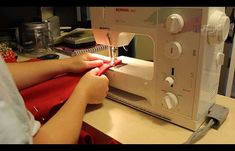 a woman is using a sewing machine to sew on something red and white fabric