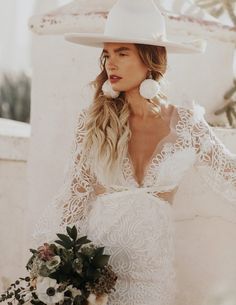 a woman wearing a white hat and dress holding a bouquet in front of her face