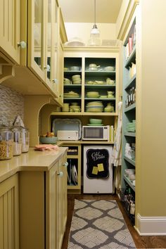 a narrow kitchen with yellow cabinets and shelves filled with plates, bowls and pans