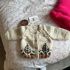 a knitted sweater with trees on it sits on a bed next to a pink pillow