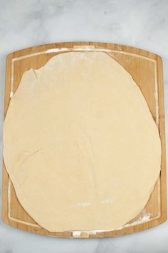 a wooden cutting board topped with uncooked pizza dough