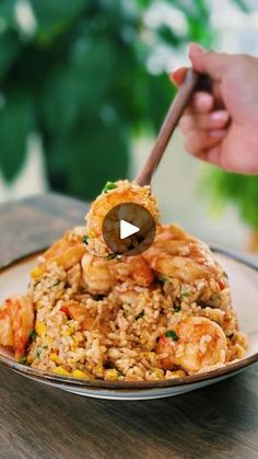 a plate with rice and shrimp on it, being held by a person holding a wooden spoon