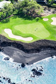 an aerial view of a golf course on the ocean with black sand and green grass