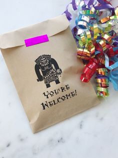 a paper bag with some colorful streamers on it and a small gift bag that says you're welcome