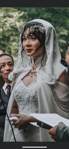 a woman in a white wedding dress and veil holding a piece of paper while standing next to other people