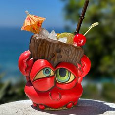 a red cup with an umbrella and some fruit in it sitting on a rock next to the ocean