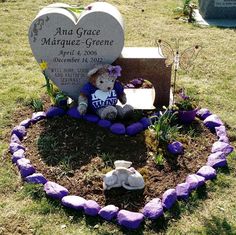 a teddy bear sitting in the middle of a grave surrounded by purple rocks and flowers