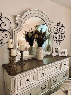 a white dresser topped with a mirror and vase filled with flowers on top of it