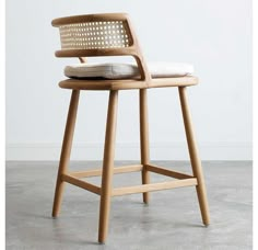 a wooden stool with a woven seat and backrest on concrete flooring, in front of a white wall