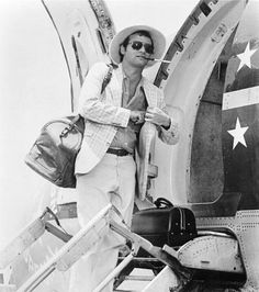 a black and white photo of a man standing on the steps of an airplane