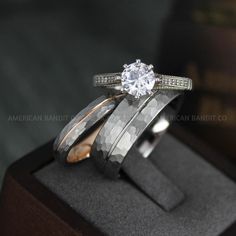 an engagement ring set with two bands and a round diamond in the center, on top of a wooden box