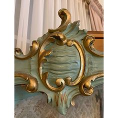 an ornate gold and green mirror frame in front of a window with curtains behind it