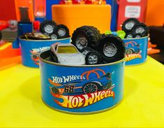 toy wheels are in a blue tin on a yellow tablecloth with other toys behind it