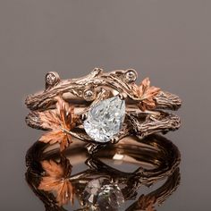 two rings with leaves and a diamond in them on top of a reflective surface, against a dark background