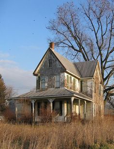 an old abandoned house sits in the middle of a field with tall grass and bare trees