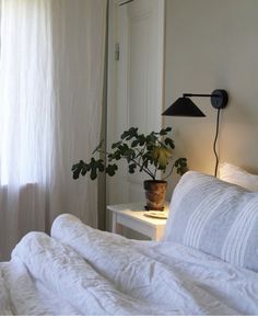 a bed with white sheets and a potted plant on the side table next to it