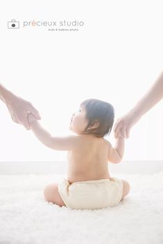 a baby sitting on the floor with his mother's hands holding him out for him