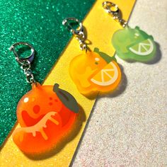 two key chains that are shaped like fruits on a yellow and green striped line with glitter behind them