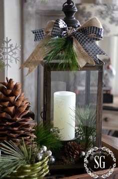 a lantern with pine cones, evergreens and a candle is on top of a table