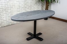 a round wooden table sitting in front of a brick wall next to a potted plant