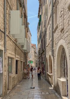 people are walking down an alley way in the old town with stone buildings and cobblestone streets