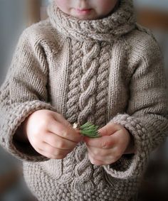 a little boy wearing a knitted sweater and holding a small plant in his hands