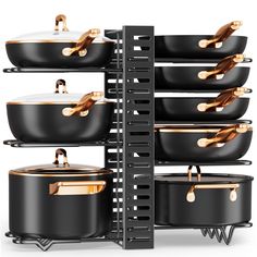 black pots and pans are stacked up on a rack with gold accents in front of a white background