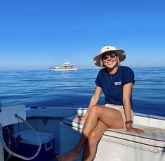 a woman sitting on the back of a boat in the ocean with a small boat behind her