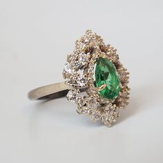 A stunning pear shape emerald ring sits luxuriously in a halo of white diamonds. Reminding us of a dark Forest Queen sparkling under the sunlight after a light forest rain. Encrusted with almost 1 carat of natural white diamonds, this ring is the epitome of royal class. Available in your choice of 14K and 18K yellow gold, rose gold or white gold. Handcrafted in NYC. 14K or 18K solid gold 2mm ring band 8x5mm Natural emerald center stone. Approx 1ct carat weight SI clarity white diamonds. Ranging Forest Queen, Forest Rain, Light Forest, Emerald Diamond Ring, Dark Forest, Natural Emerald, Emerald Diamond, Emerald Ring, White Diamonds