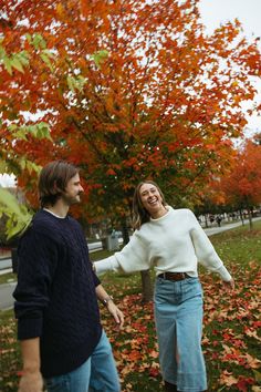 a man and woman are walking through the leaves