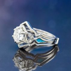 a diamond and blue stone ring sitting on top of a reflective surface with its reflection