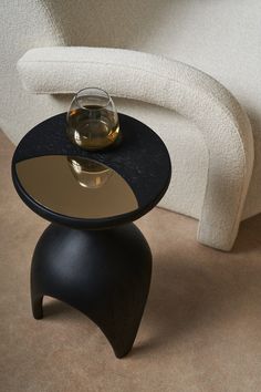 a black table with a wine glass on it and a white chair in the background