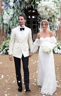 a bride and groom holding hands in front of an archway decorated with white flowers at their wedding