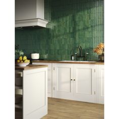 a kitchen with green tiles on the wall and white cabinets in front of the sink