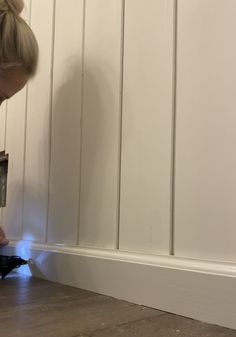 a woman is painting a wall with white paint and a light on the floor in front of her