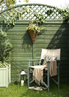 a chair sitting in the grass next to a wooden fence and potted planter