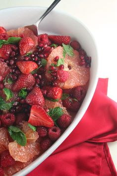 a white bowl filled with fruit on top of a red cloth next to a spoon