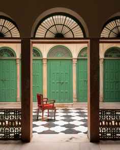 a red chair sitting on top of a checkered floor in front of green doors