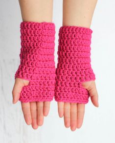 a woman's hand wearing pink crocheted arm warmers with thumb holes