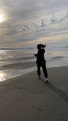 a woman standing on top of a sandy beach next to the ocean under a cloudy sky