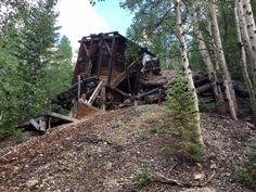 an old wooden structure sitting on top of a hill surrounded by trees and rocks in the woods