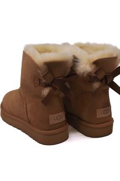 Experience a touch of elegance with our iconic UGG® Mini Bailey Bow II Chestnut, now adorned with silky bows for a charming and feminine touch. Made with luxurious sheepskin, this versatile boot boasts a durable yet lightweight sole for added comfort and grip. A staple for any fashionista's wardrobe, this boot is sure to be a fan favorite!

This product was made in a factory that supports women in our supply chain with the help of HERproject, a collaborative initiative that creates partnerships with brands like ours to empower and educate women in the workplace. Uggs With Bows On The Back, Ugg Bailey Bow Mini, Bow Uggs, Ugg Mini Bailey Bow, Ugg Boots With Bows, Ugg Bailey Boots, Cute Uggs, Ugg Mini Bailey, Women In The Workplace