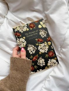 a woman's hand holding a book on top of a white bed with flowers