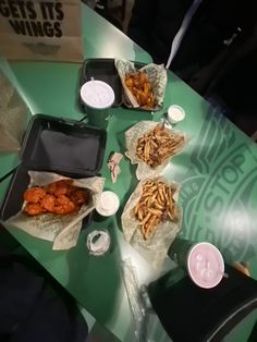 several trays of food sitting on a green table with white cups and napkins