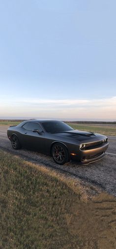 a black sports car driving down a road next to a grass covered field on a sunny day