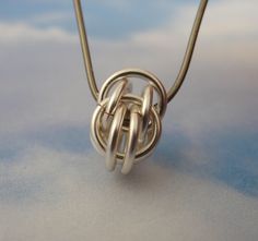 a silver necklace on a white surface with clouds in the backgroung area