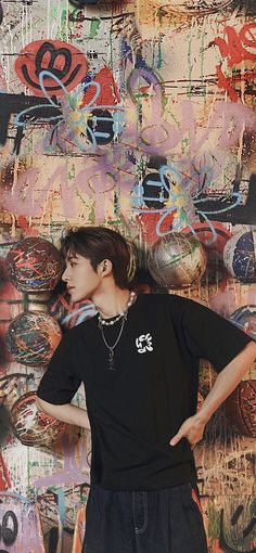 a young man standing in front of a wall covered with graffiti and other art work