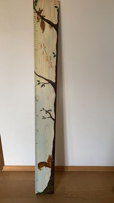 a tall wooden ruler sitting on top of a floor next to a wall with a tree painted on it