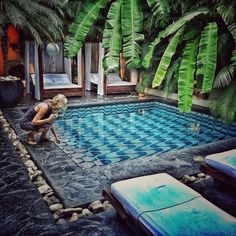 a woman kneeling down in front of a pool surrounded by palm trees and lounge chairs